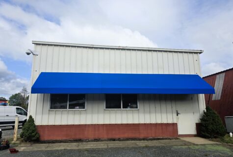Photo of bright blue awning affixed to corrugated metal building in Stafford, VA. Awning was manufactured & installed by Distinct Sign Solutions in Fredericksburg, VA