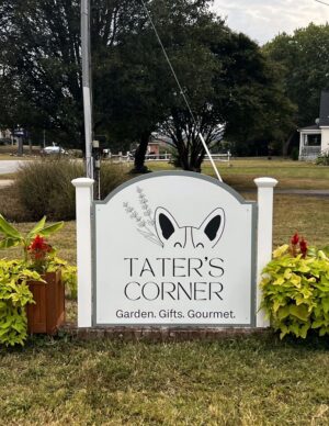 Photo of white and sage green sign with PVC wrapped posts sitting in between floral arrangements in Stafford, VA. Sign was manufactured and installed for Tater's Corner by Distinct Sign Solutions in Fredericksburg, VA