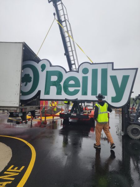 Large commercial O’Reilly Auto Parts sign being lifted into place by crane during professional sign installation.