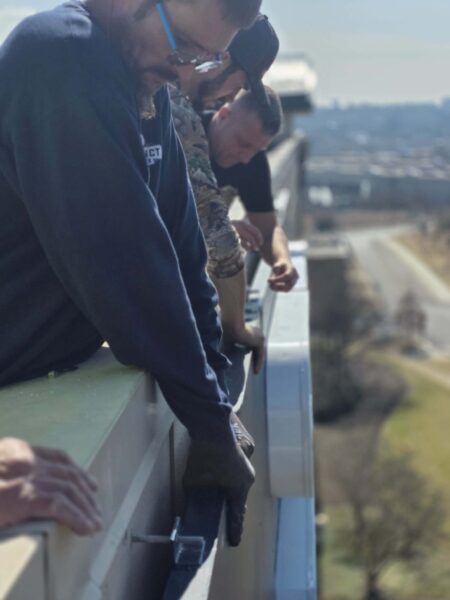 Sign installation technicians securing a large building sign along the roofline of a commercial property.